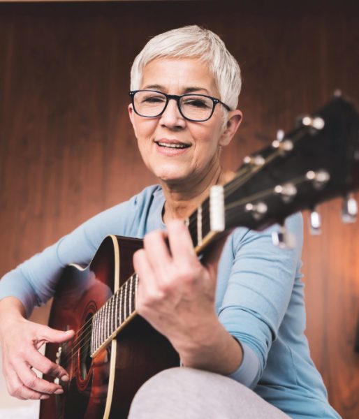 Portrait of beautiful mature woman playing guitar in cosy modern apartment, Free time hobbies music and art concept