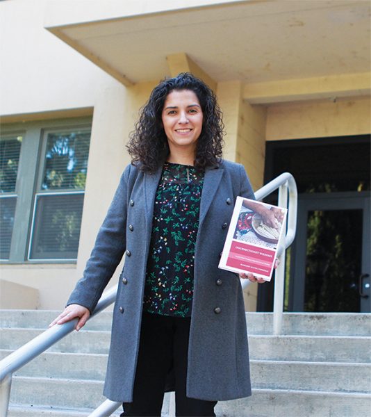 La Dra. Marlene Ferreras posa con una copia de su libro en los escalones de La Sierra Hall, que alberga la H.M.S. Richards Divinity School donde enseña.