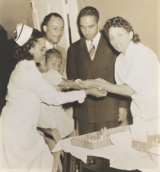 Dr. Temple administers vaccine. Looking on 
is Dr. Owen A. Troy (left), president of the Community Health Association.<br /><em>Photo courtesy of Dr. Carmelita Troy</em>.